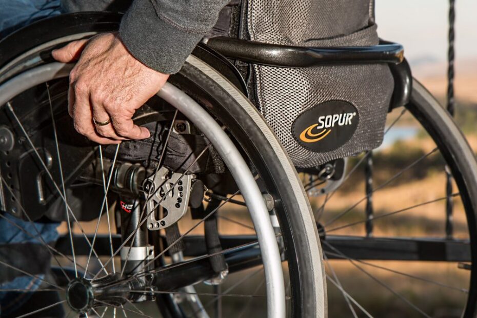 Close-up van een rolstoel van de zijkant gezien. Een deel van het wiel is zichtbaar en de hand van degene die in de rolstoel zit.