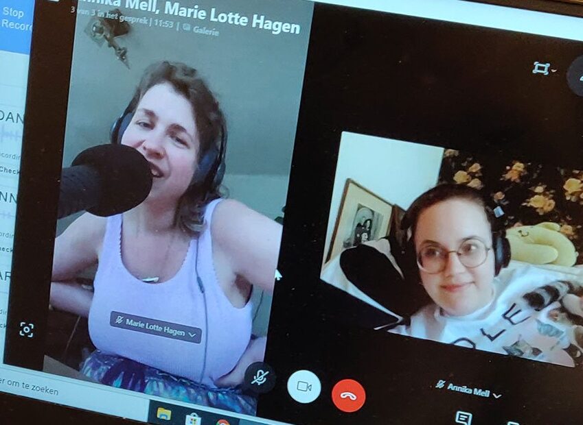 Foto van een laptop waarop Skype is geopend. Links op het scherm is Marie Lotte, een witte vrouw met een witte top en halflang donker haar in beeld, rechts is Annika in beeld, een witte vrouw met een bril en een koptelefoon op.